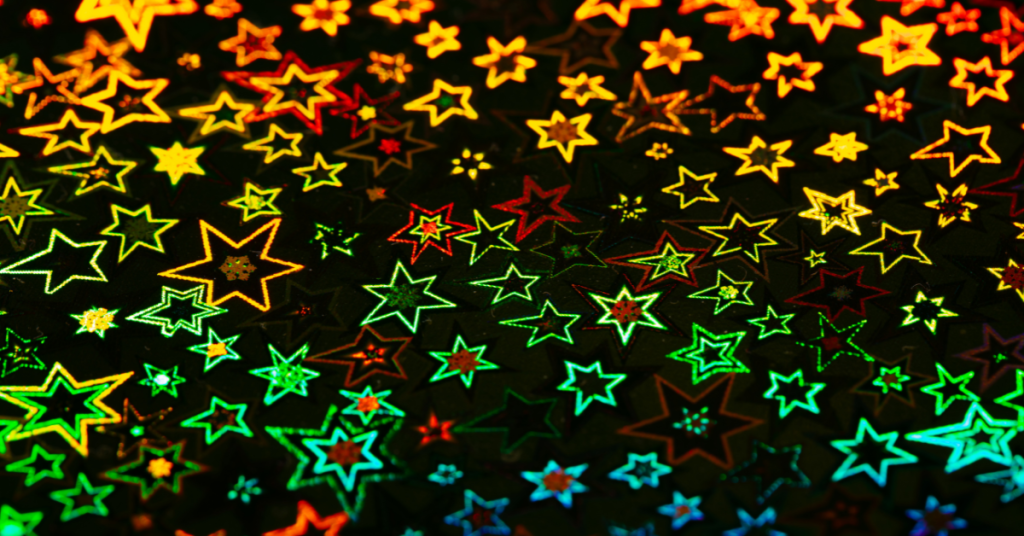 Colorful holographic stars in green, red, and yellow on a dark background. The stars vary in size, creating a vibrant, festive pattern.